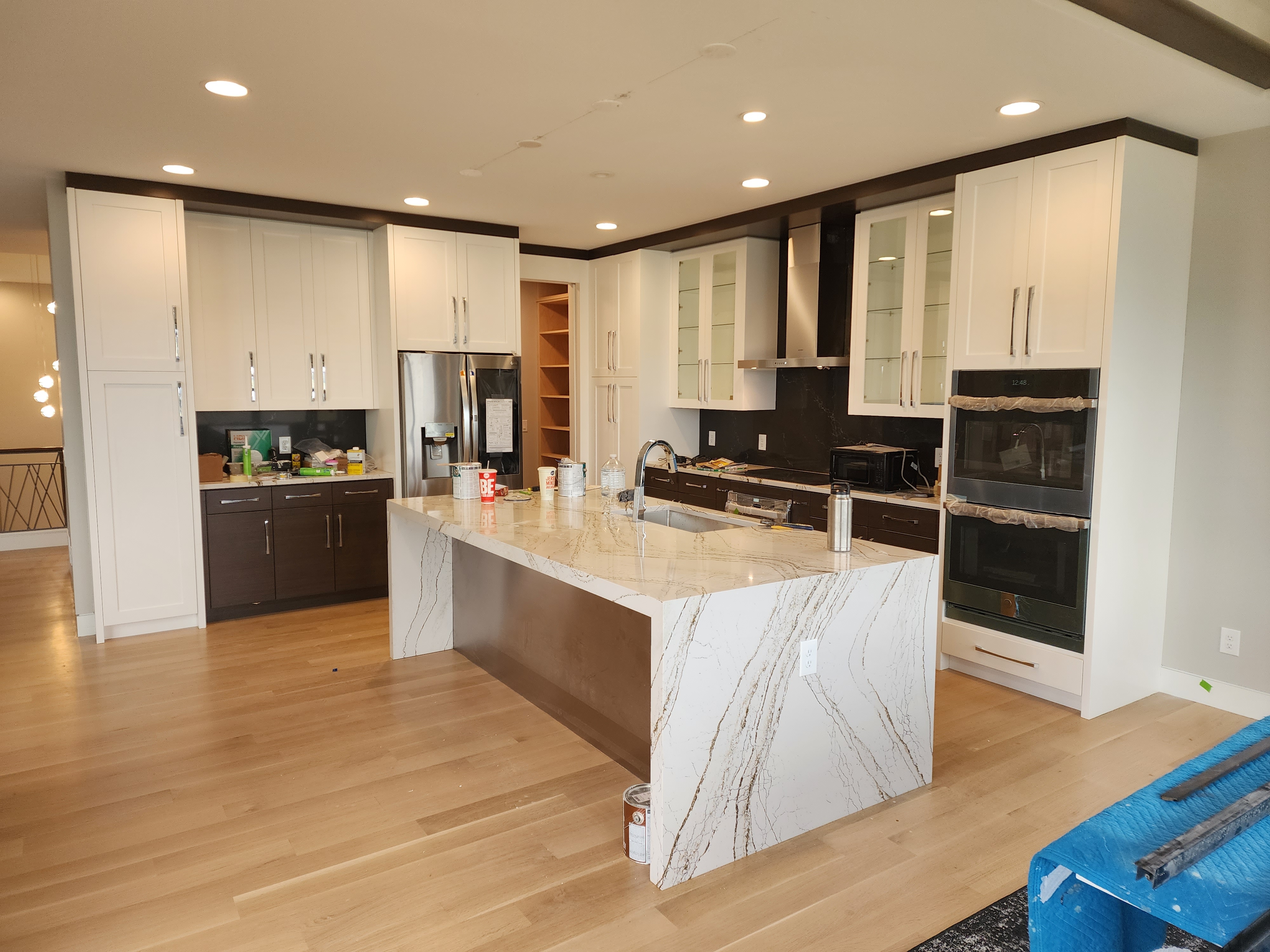 Open kitchen with white shaker cabinets, dark espresso base cabinets, and a dramatic marble waterfall island