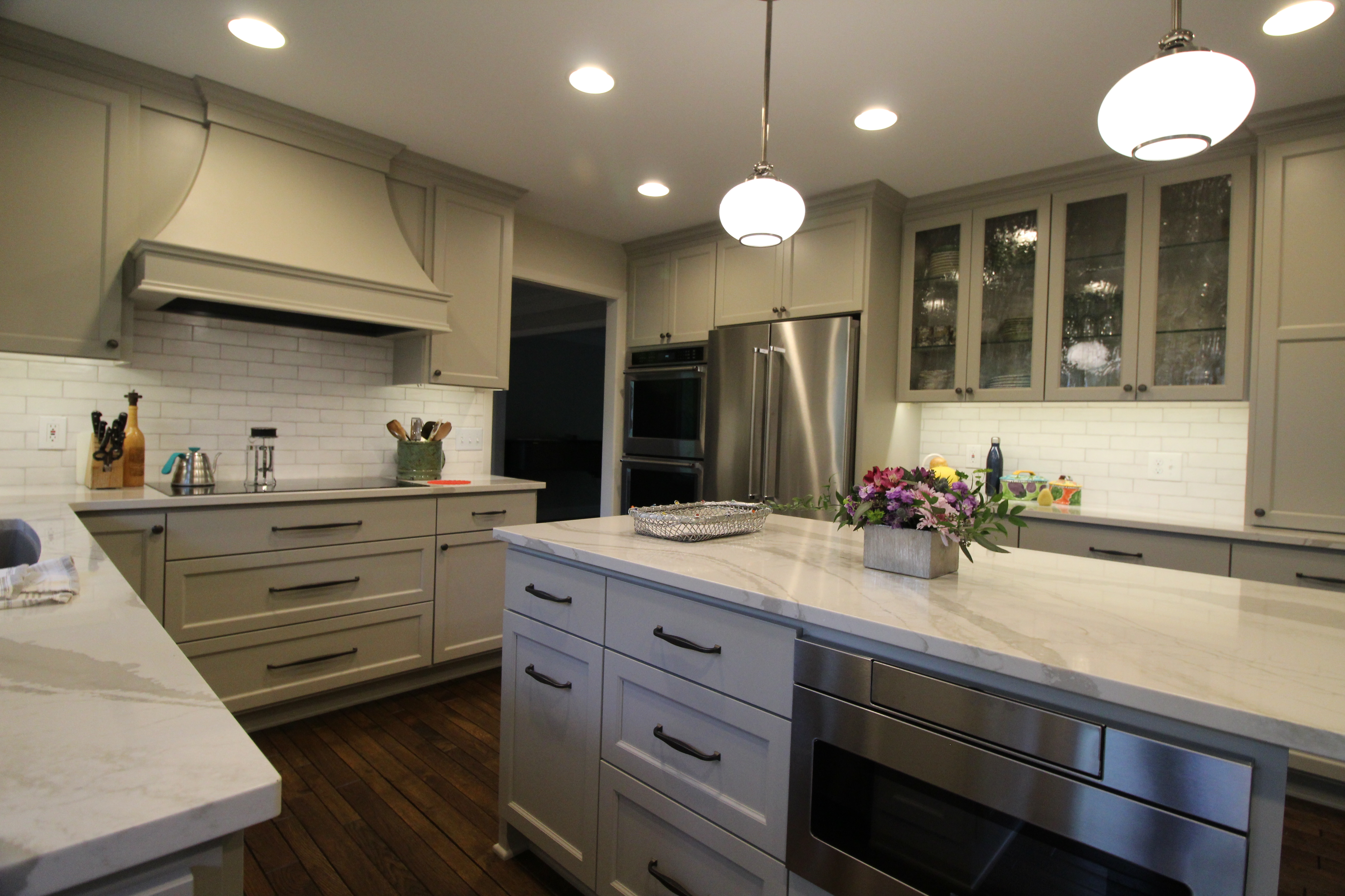 Range wall with custom hood, subway tile, and built-in ovens in the island