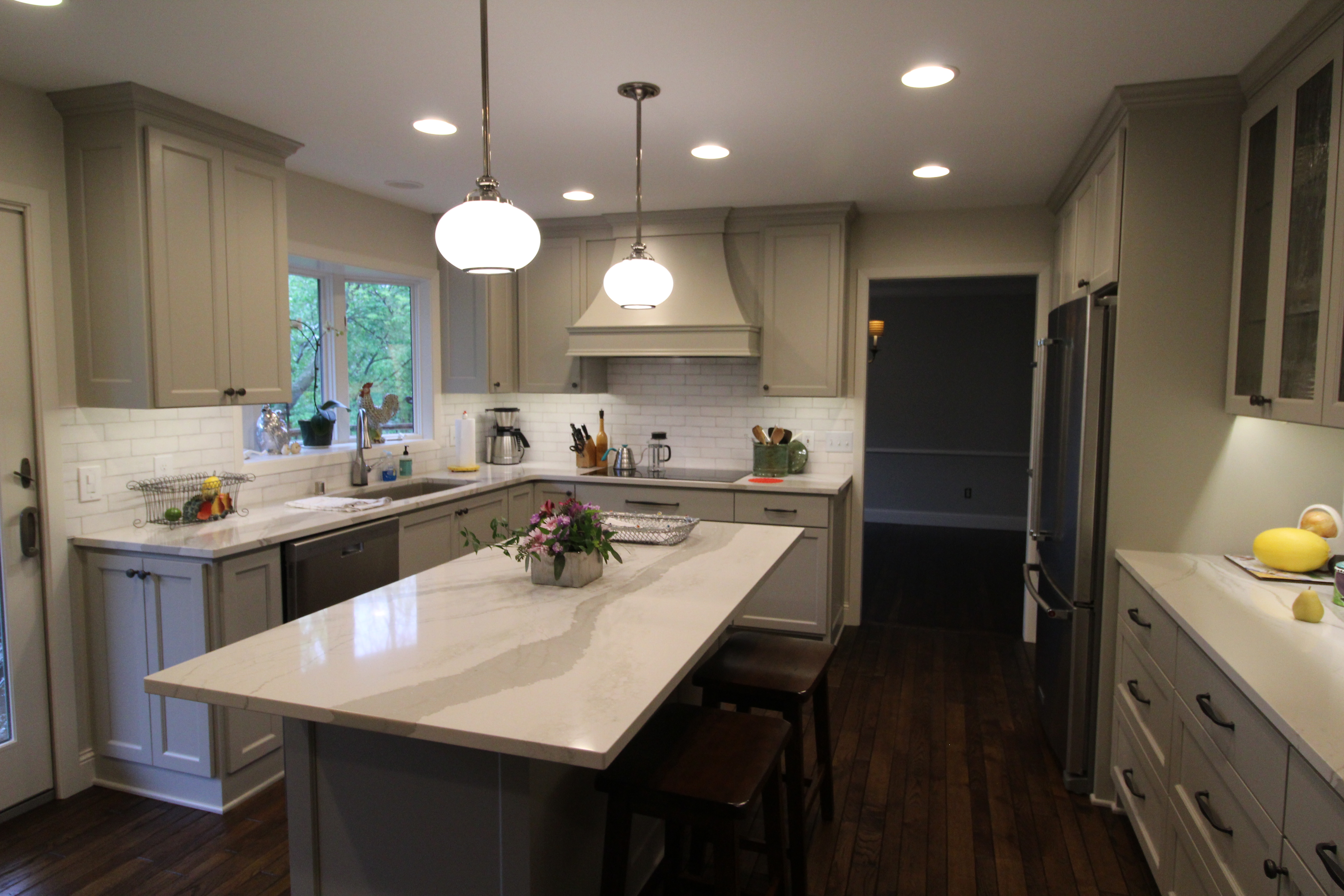 Sage-gray shaker kitchen with marble waterfall island, pendant lights, and subway-tile backsplash