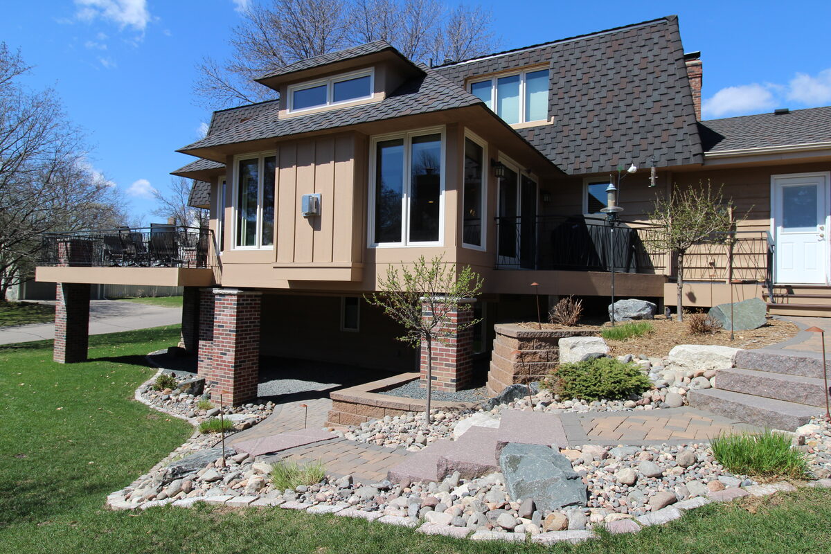 Exterior of a two-story home addition with brick base, wood siding, and a covered deck