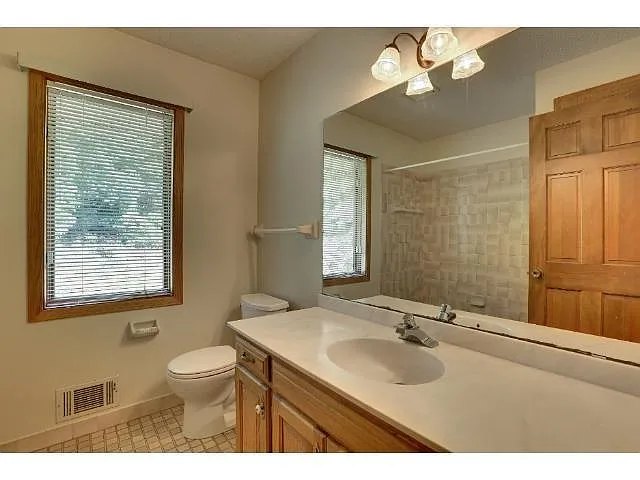 Existing bathroom with wood cabinetry, a wide mirror and a window beside the toilet.