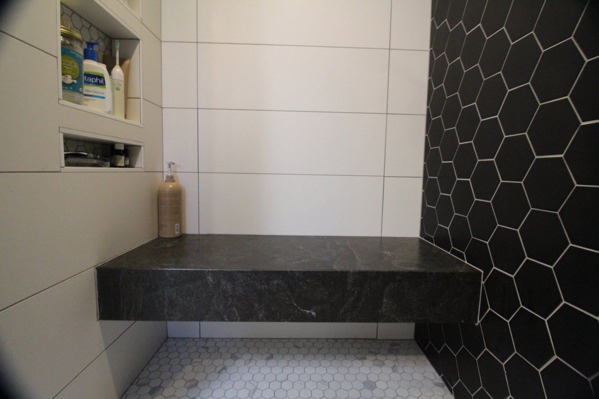 Floating shower bench between a tiled niche wall and a black hexagonal tile wall.