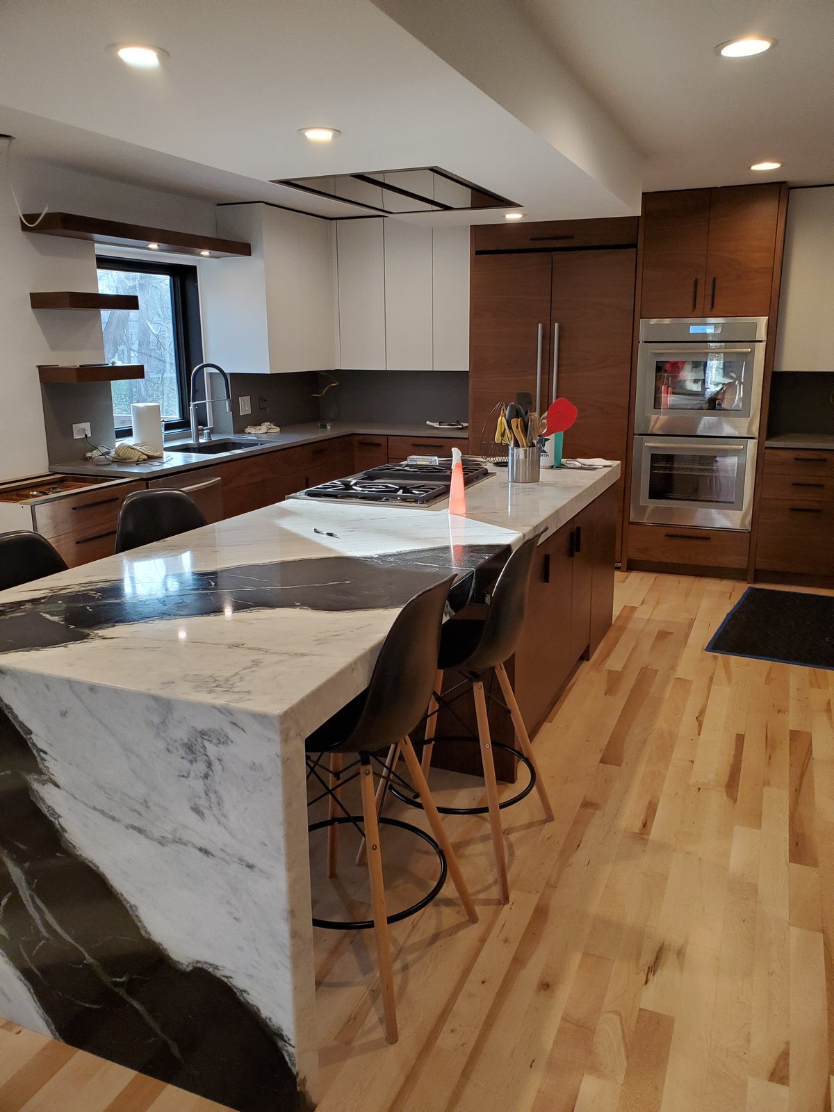 Kitchen near completion with a stone waterfall island, white upper cabinets and walnut cabinetry.