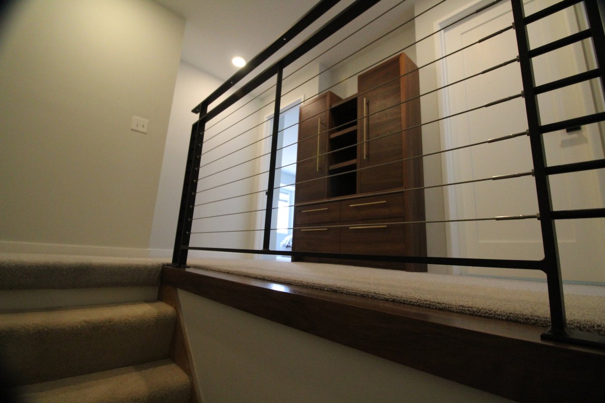 Black posts and horizontal wire railing beside a carpeted stair and landing.