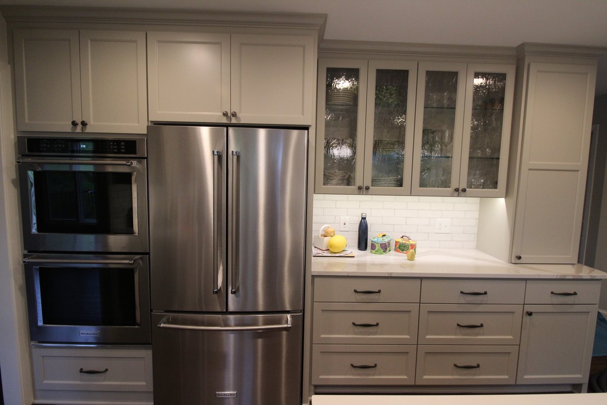 Kitchen cabinet wall with refrigerator, wall ovens and glass-front upper cabinets.