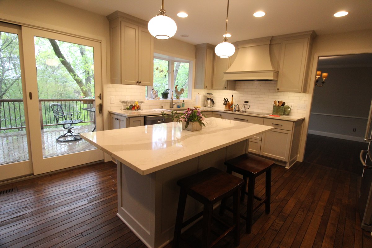 Painted kitchen cabinets and a quartz island with seating beside the sink and cooking wall.