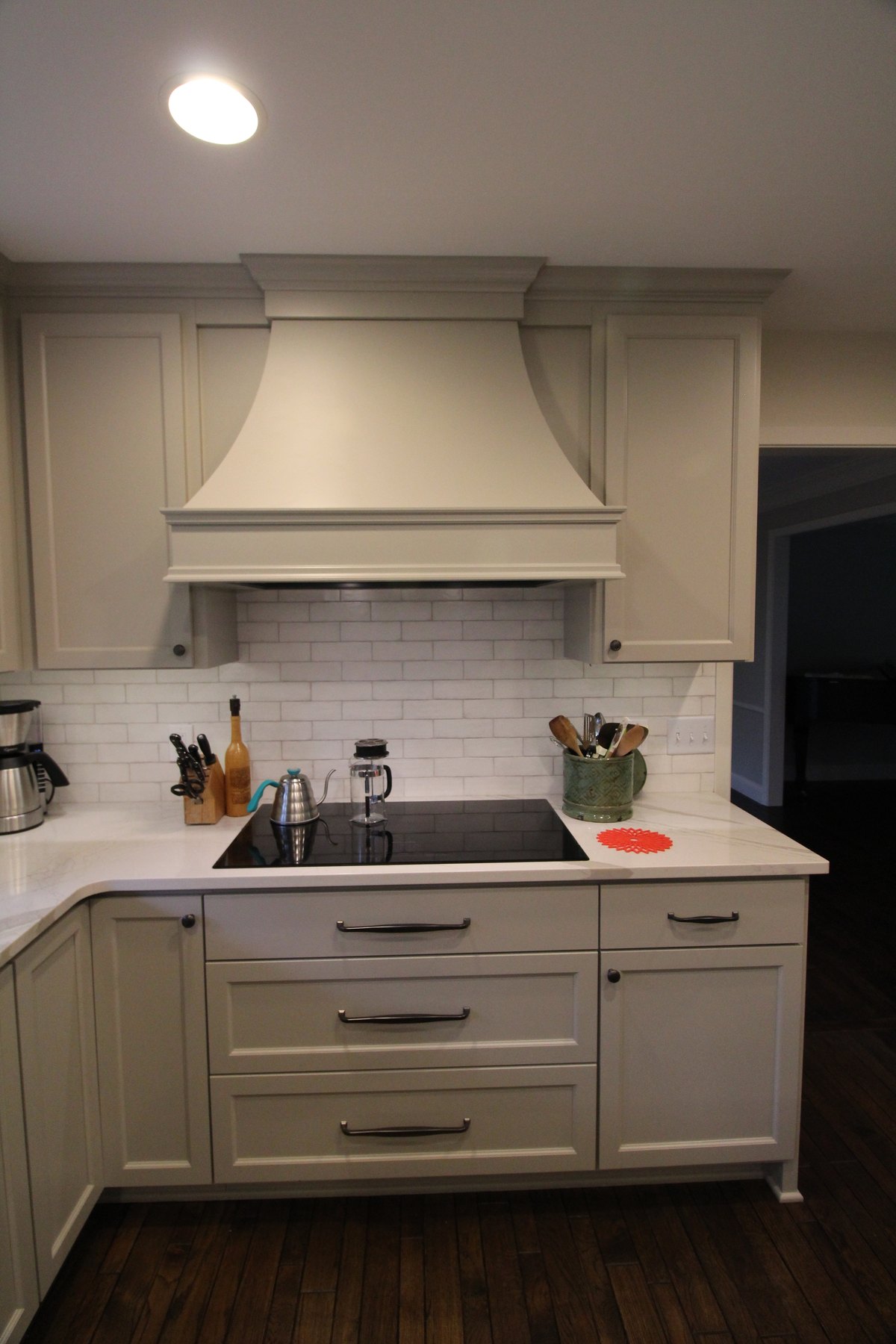 Built-in range hood above a cooktop with painted cabinets and a tiled backsplash.
