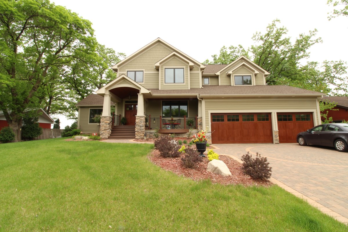 Two-story home with a covered entry, stone column bases and wood garage doors.