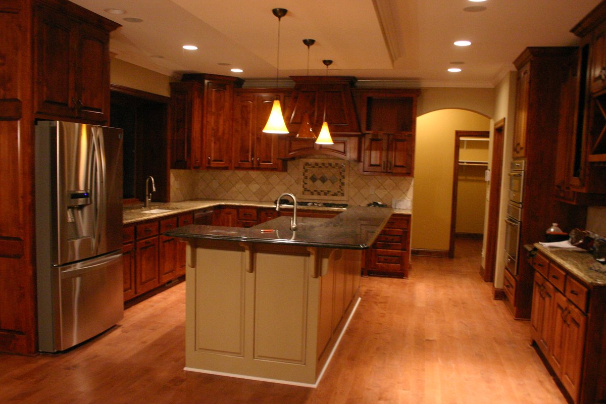 Kitchen with warm wood cabinets and a light-colored island beneath pendant lights.