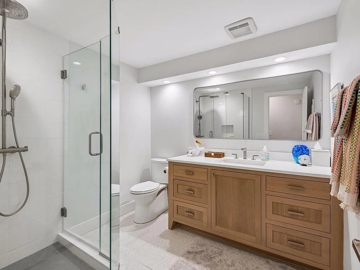 Bathroom with a wood vanity, wide mirror and glass shower enclosure.