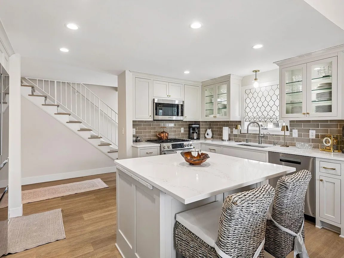 Townhome kitchen with painted cabinets, an island with two seats and stairs beside it.