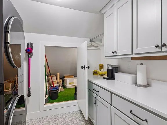 Laundry room with stacked appliances, painted cabinetry and a counter.