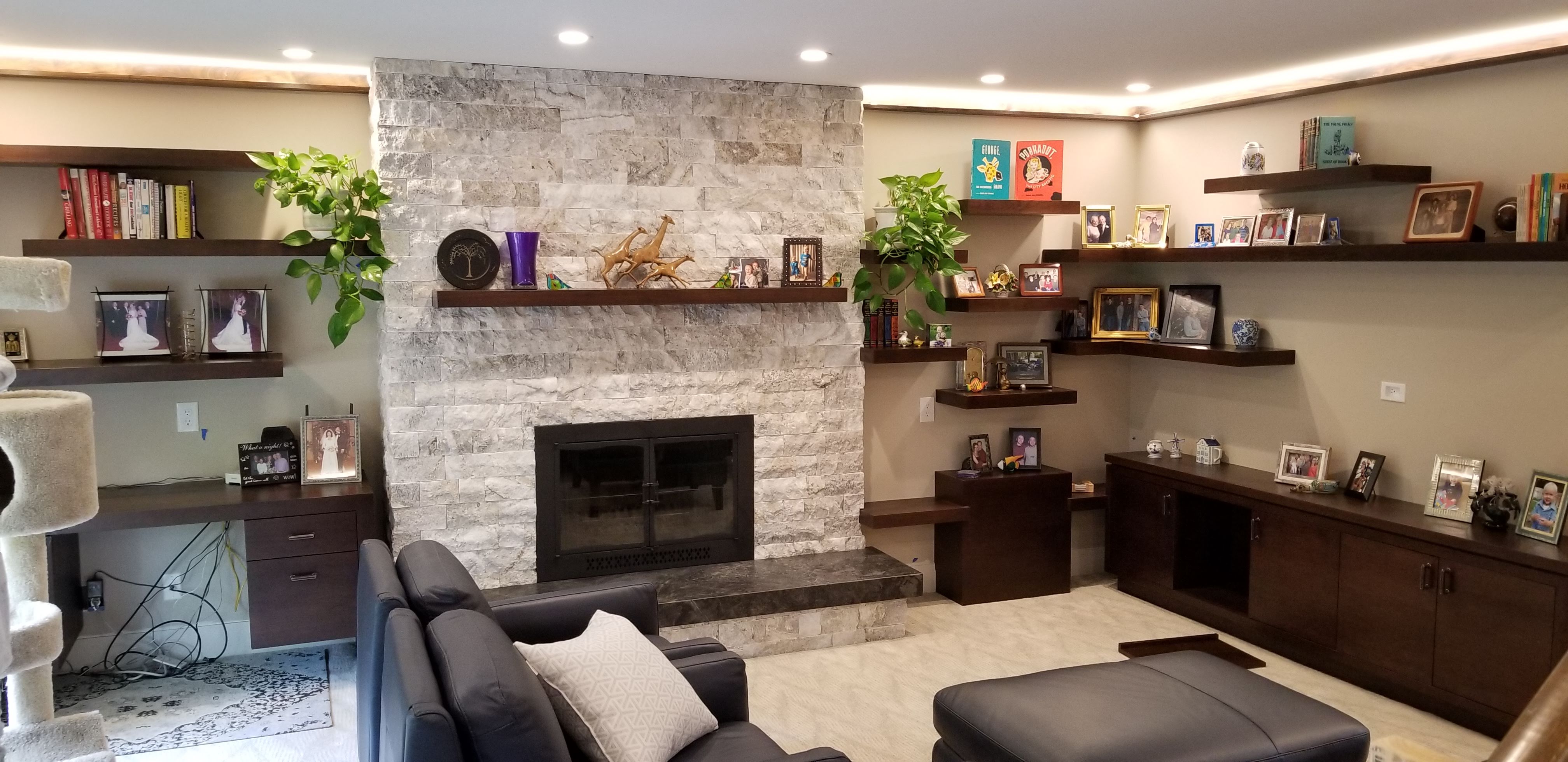 Lower-level living room with stone fireplace, custom walnut built-ins, and family photos