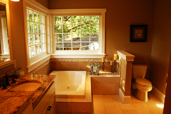 Primary bath with a drop-in tub under a divided-light window and granite-topped vanity