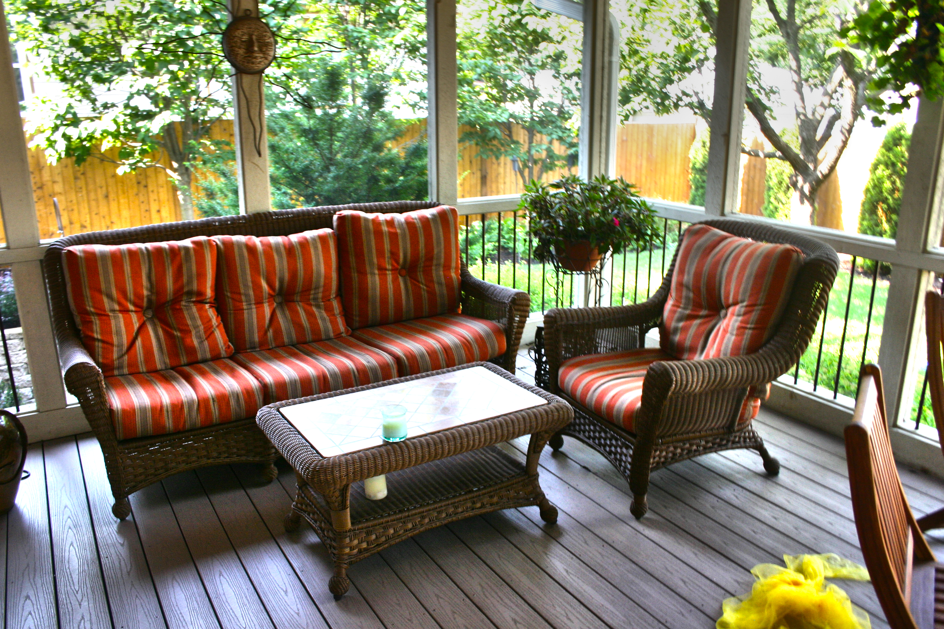 Screened porch with wicker furniture, striped cushions, and a view into the back yard