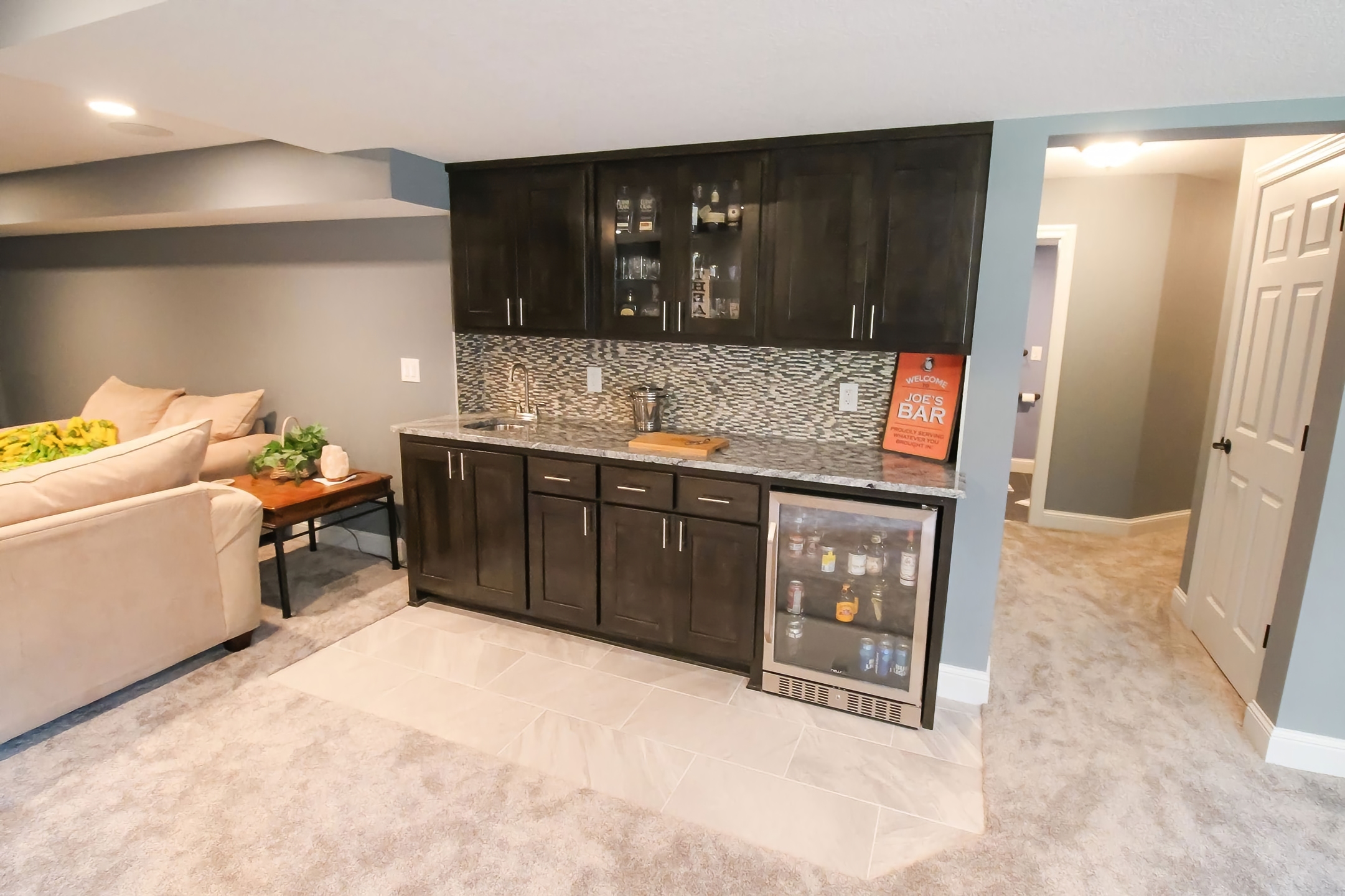 Wet bar with espresso cabinetry, mosaic tile backsplash, granite counter, and beverage fridge