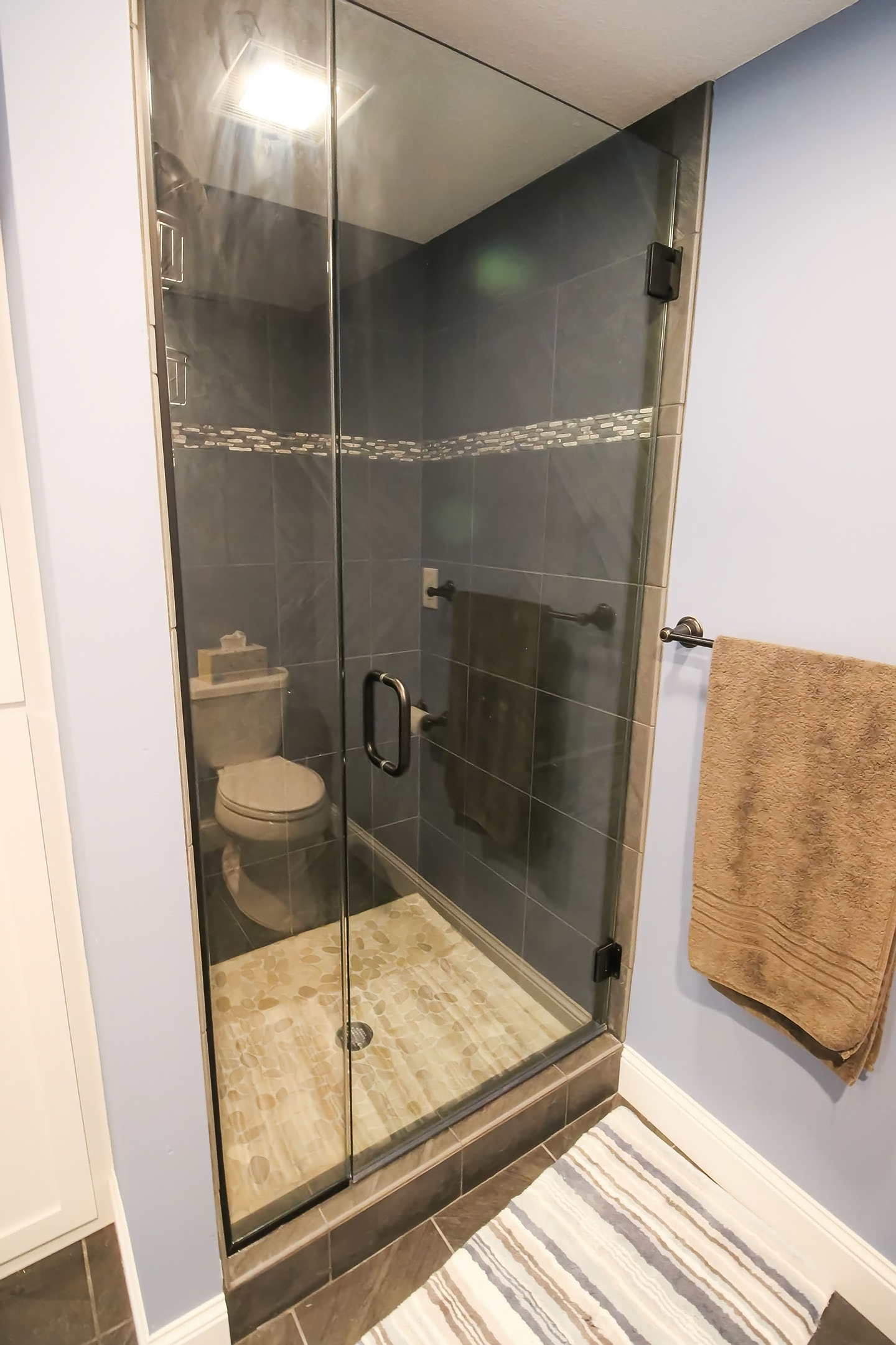 Basement full bath with dark porcelain tile, glass shower, and pebble floor
