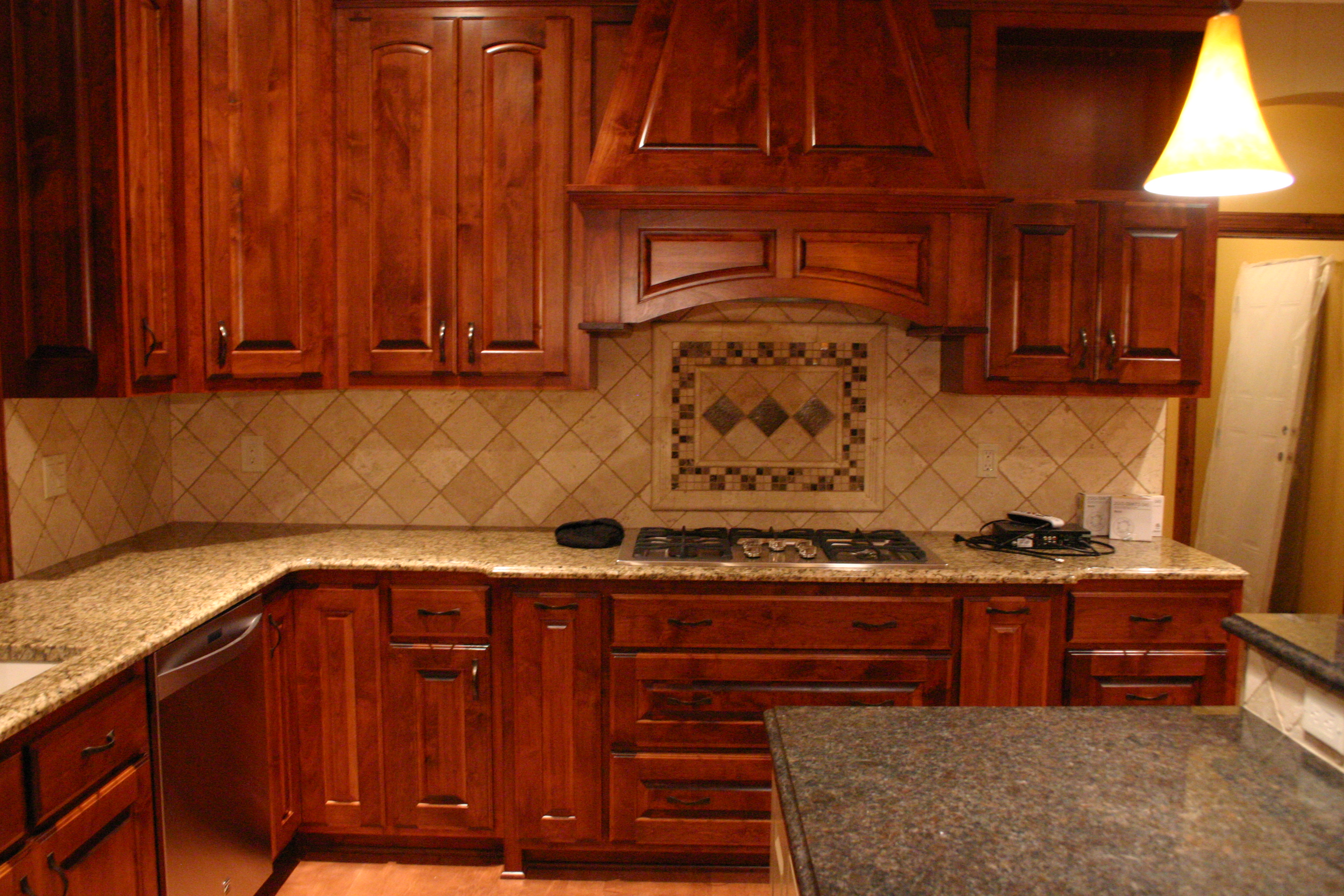 Cherry kitchen with custom hood, tile backsplash medallion, and granite counters