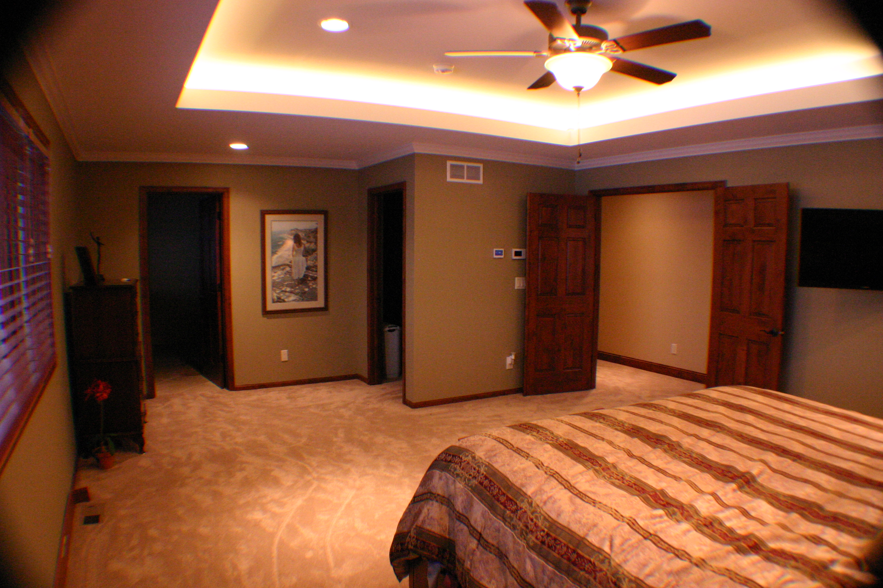 Primary bedroom with tray ceiling, rope lighting, and warm wood trim